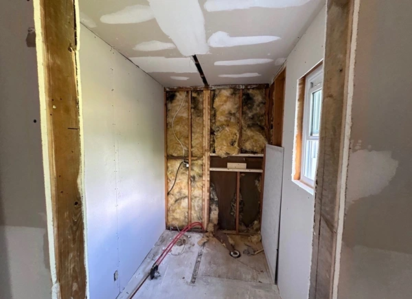 Bathroom gutted to the studs with fresh insulation and drywall during reconstruction